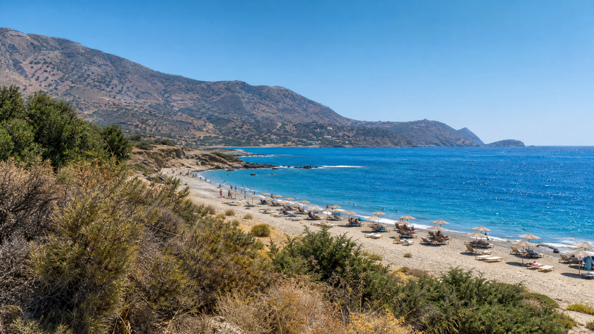 A busy Cretan beach with clear water in peak summer