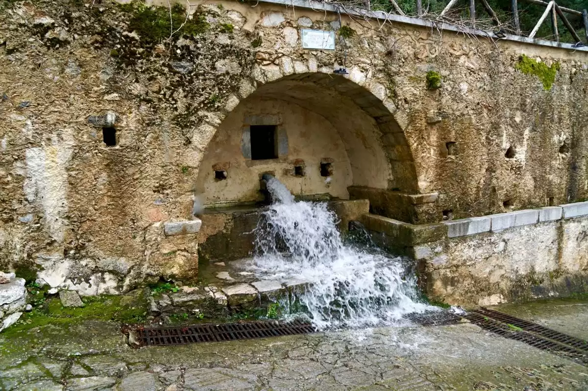 Stone fountain in Krasi with running water emerging from an arched recess